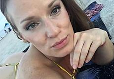 Bestial MILF Jillian Basal spooning her deep cleavage in a skimpy gold two-piece at the shore